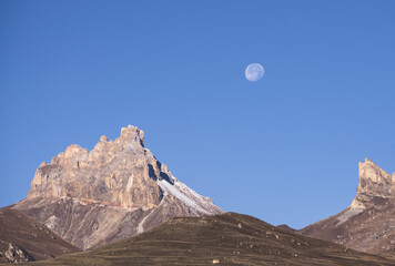 The waning moon in the mountains against the background of a blue sky with rocks and mountains, autumn in the mountains