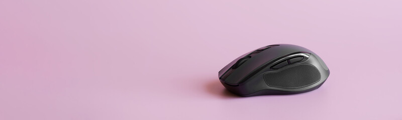 Black computer mouse with a scroll wheel, additional buttons and a rubber pad on a pink background. Copy space. Web banner.