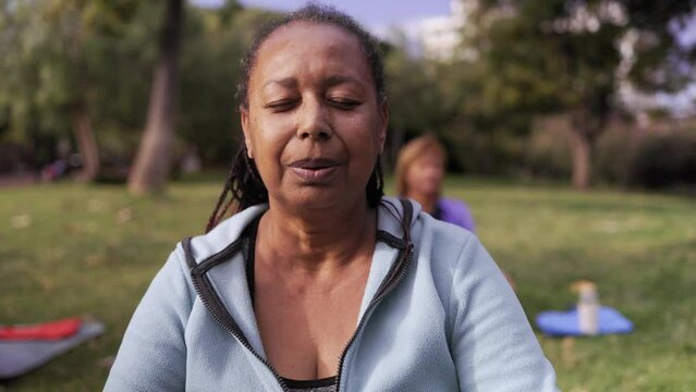 African senior woman doing yoga meditation breathing outdoors at park city - Elderly health care community