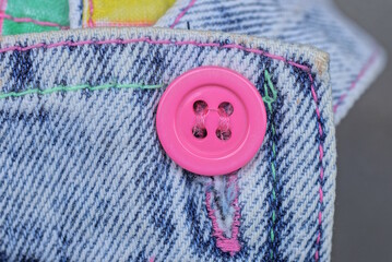 one pink plastic round button on a blue gray cotton fabric on clothes