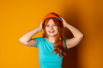 A red-haired girl wearing a construction helmet is showing a thumbs-up on an isolated orange background. Emphasizing safety regulations.