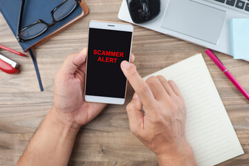 Finger of a man pointing at the SCAMMER ALERT message on the smartphone screen 