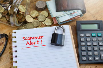 SCAMMER ALERT message was written on the notebook with a padlock, calculator, pile of coins, and cash