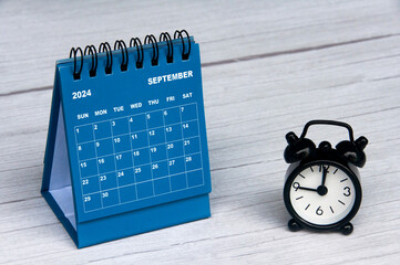 September 2024 calendar on wooden desk and alarm clock with customizable space for text. Monthly calendar concept and copy space.