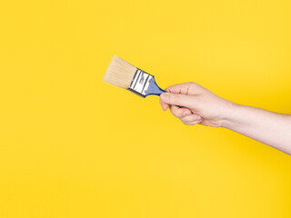 Hand with a paintbrush. Yellow background, no face.