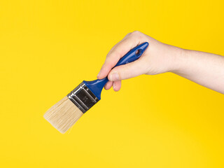 Hand holding a paintbrush. Yellow background, no face.
