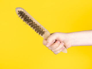 Hand holding a steel brush. Isolated on yellow background, no face.
