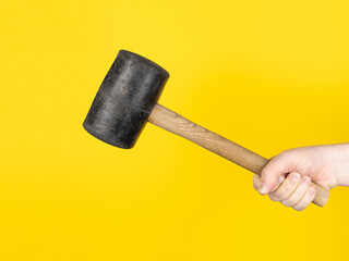 A hand is holding a rubber mallet against a yellow background. No face, copy space, concept.