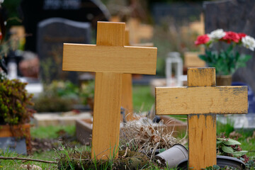 simple wooden crosses on graves of a cemetery in front of blurred background with flowers and...