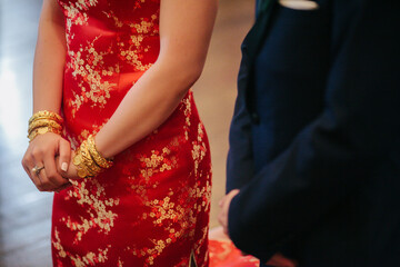 torsos of groom in suit and bride in traditional red dress with gold bracelets at wedding tea ceremony 