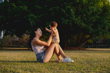 "Millennial Mom with Curious Baby on Urban Park Lawn"

