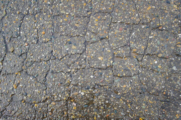Old road background surface of gray cracked asphalt texture closeup. Old cracked asphalt. Grunge background. Wet