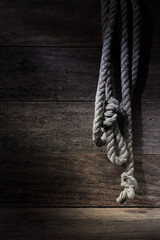 Old frayed grey length of rope hanging down rustic wooden setting soft dark mood lighting copy space 