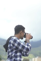 Young man traveler photographer taking pictures in nature with his camera vertical copy space