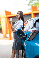 Woman standing holding a cup of coffee while waiting to charge an electric car at a city public charger station