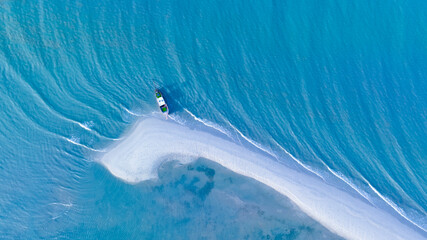 High-angle shot of a long-tailed boat parked on a white beach with beautiful sea waves.