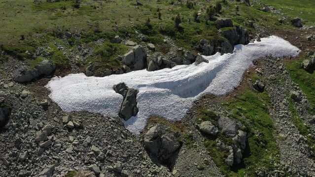 Aerial video of mount Sarlyk slopes. Drone flies along slope with snowfield and rocks. Altai highlands.