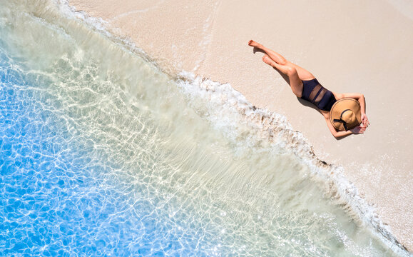 Aerial view of beautiful young woman in black swimsuit lying on sandy beach near blue sea with waves at sunset Summer vacation at Andaman Island