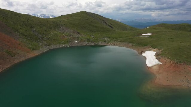 Aerial video of Mountain Spirits Lake in Altai mountains. Herd of horses hides from horseflies on a snowfield.