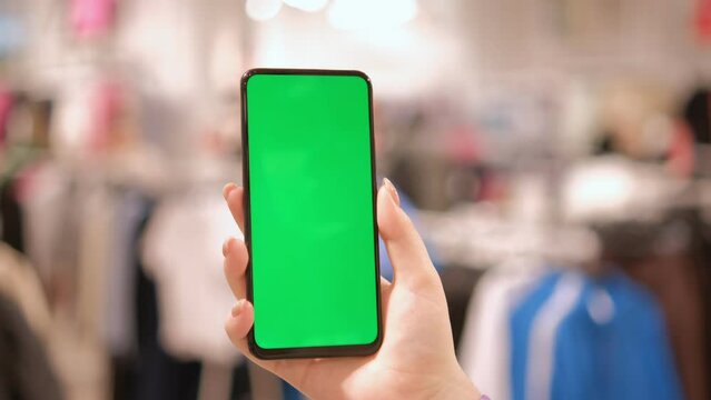 A young girl holds a phone with a green screen. Mall. Use green screen for copy space closeup. Chroma key mock-up on smartphone in hand. hold mobile phone and looking photos or pictures