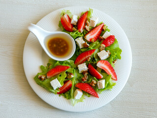 Plate of homemade fresh summer sliced Strawberry and lettuce salad with feta cheese and walnuts. Organic healthy diet, vegetarian salad food. Top view.