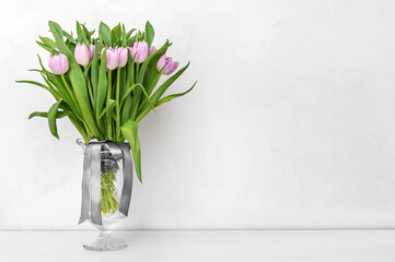 Vase with bouquet of freshes beautiful tulips on the table near wall. Copy space.