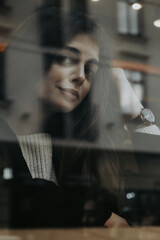 girl in dark jacket and a white sweater behind a cafe window