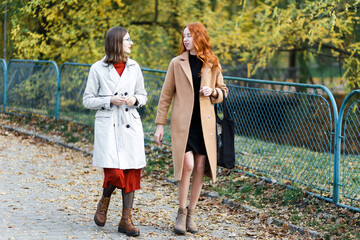 two young women in coats walked through the park in autumn