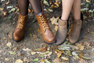 legs in stylish leather brown boots on the background of autumn leaves