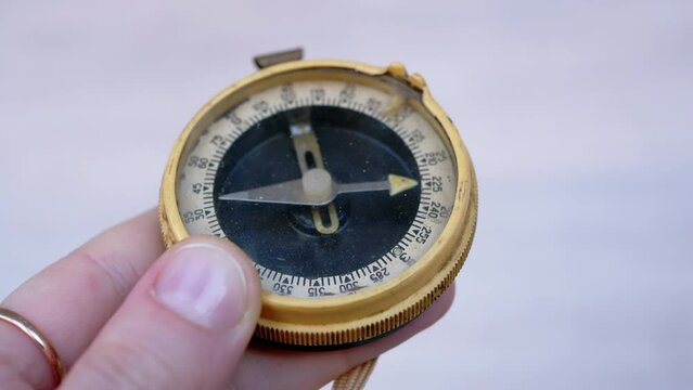 Woman Examining an Old Dirty Dusty Compass in her Hand Indoors. An antique old compass that has fallen into disuse. White background. Direction search. Magnetic needle. Location orientation. Travel.