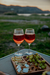 Picnic in nature with wine, cheese plate, grapes with mountains and sunset in the background