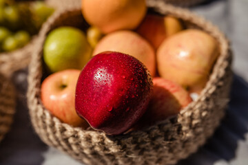 red apple with drops of water and dew lies in a wicker basket in the summer at a picnic