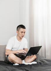 Asian man is using laptop on the bed in bedroom.