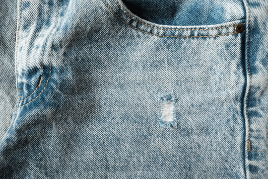 Hole and Threads on Denim Jeans. Ripped Destroyed Torn Blue jeans background. Close up blue jean texture.