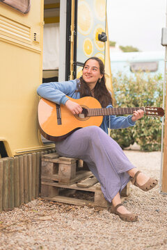 Young woman playing guitar at a campsite.