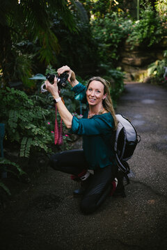 Woman with camera and backpack in green lush forest photographing