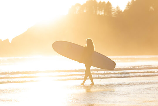 Surfer walking her board out to the beach at sunset along Oregon Coast