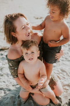 Laughing mother holding twin toddler boys in the sand