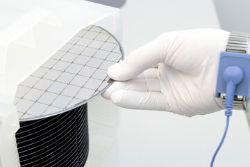 Gloved Hand Holding a Silicon Wafer in plastic holder box used in electronics for the fabrication of integrated circuits. Silicon wafer inspection.