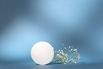 Abstract empty white podium with shadows and white flowers on blue background. Minimal concept. Podium for cosmetic product presentation. Abstract minimal geometrical form. Cylinder podium with shadow
