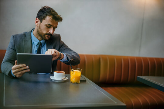 Busy young businessman checking the time on his watch and using a digital tablet computer in the modern business lounge.