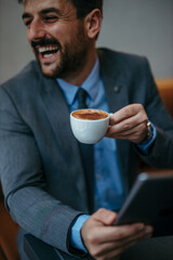 Portrait of a smiling bearded young man drinking coffee and looking aside in a cafe.