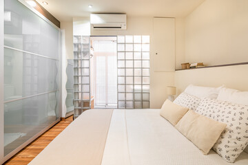 Original design of bright small bedroom with glass wall in the bathroom and glass rack. Concept of an unusual interior and a compact room. Hotel room