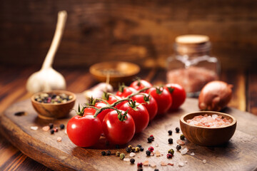 Małe czerwone pomidorki z przyprawami na drewnianym stole - obrazy, fototapety, plakaty