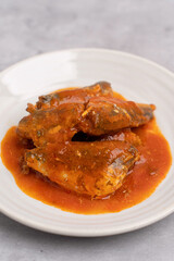 Canned fish. Mackerel in tomato sauce in a white plate on a concrete table.