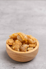 Pork rind. Crispy pork rinds are made from fine pork skin in a wooden bowl on a cement table.
