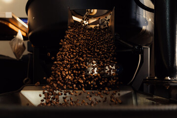 Roasted coffee beans pouring from release chute in modern factory