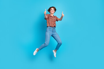 Fototapeta na wymiar Full body portrait of carefree cheerful lady jumping demonstrate thumb up isolated on blue color background