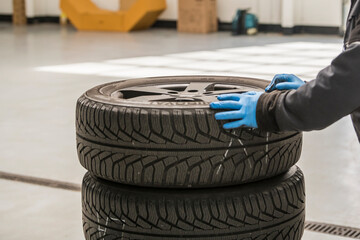 Selective focus. Close-up of 2 hands with blue glove pushing a trolley with car tires r in a garage...