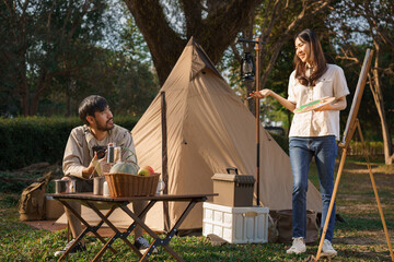 Camping concept, Young couple doing activity outside tent to painting on canvas and taking a photo